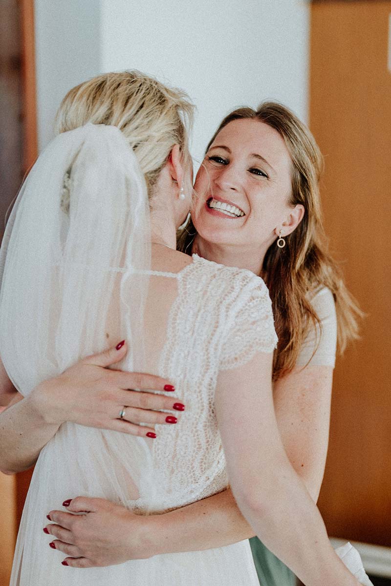 Braut umarmt eine Freundin kurz vor der freien Trauung auf Rügen, beide lächeln herzlich