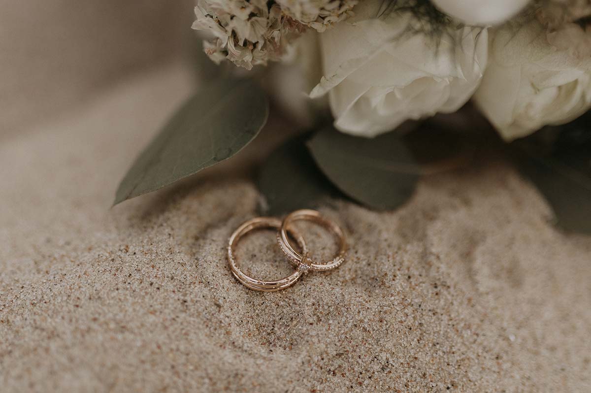 Zwei Eheringe liegen im Sand, umgeben von weißen Rosen – Symbolfoto einer freien Trauung auf Rügen