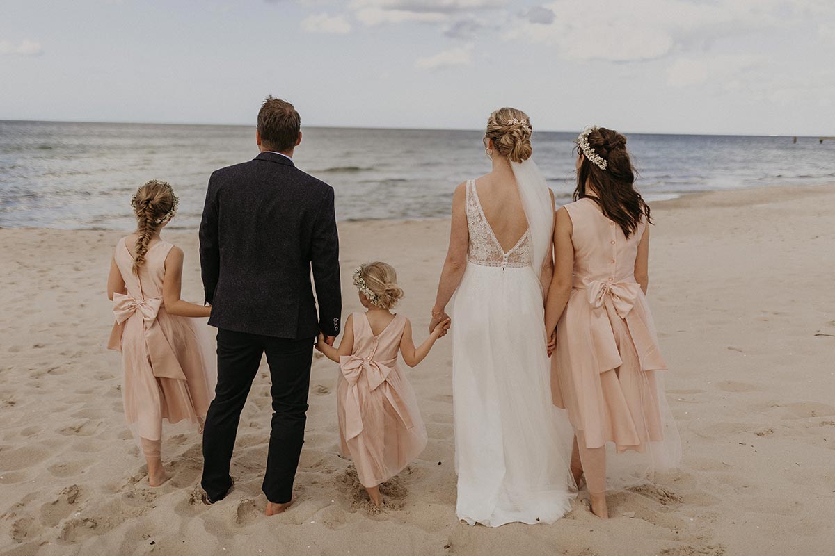 Brautpaar mit zwei Blumenmädchen steht Hand in Hand am Strand von Rügen bei einer freien Trauung